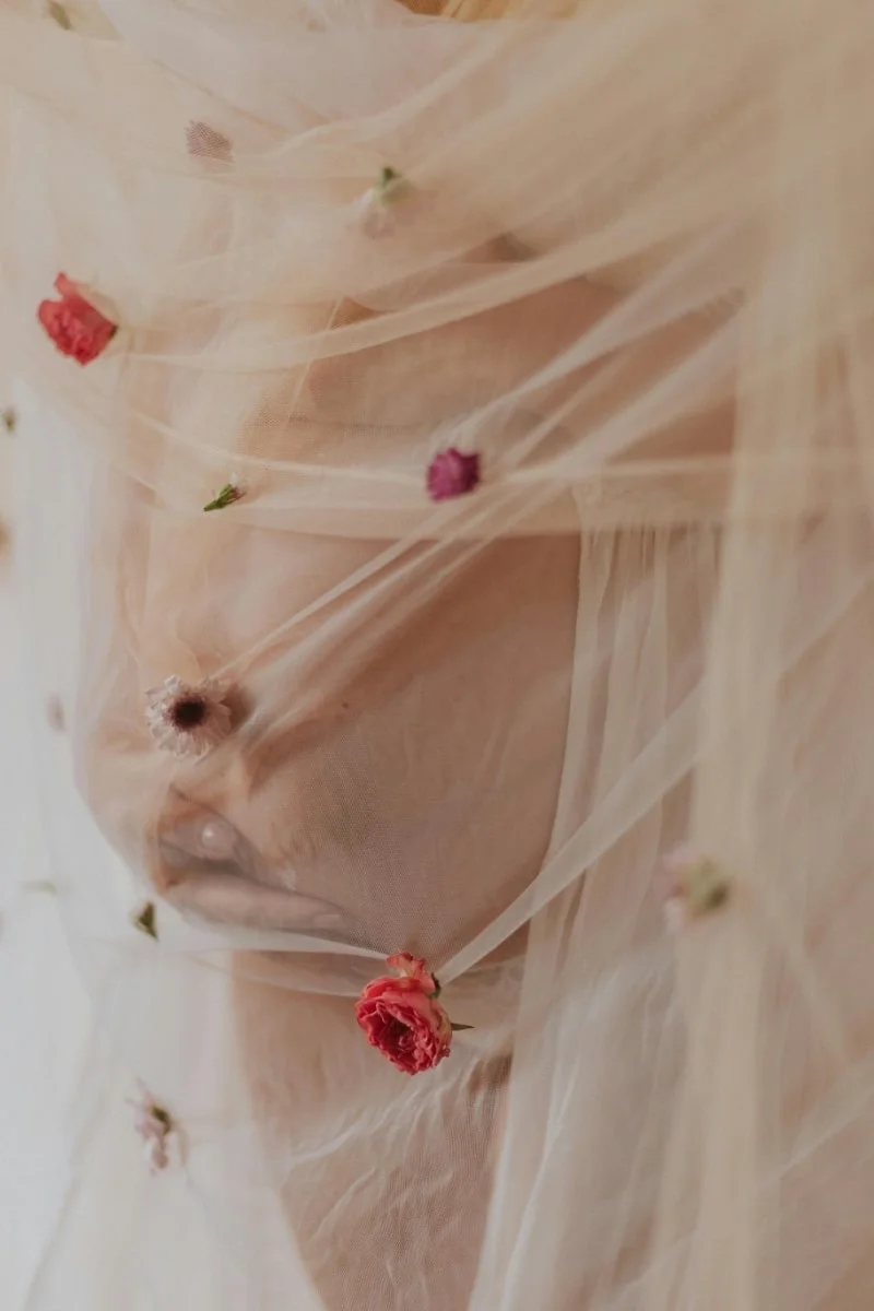 femme enceinte sous un voilage et des fleurs-min une femme enceinte qui tient son ventre dans la pénombre